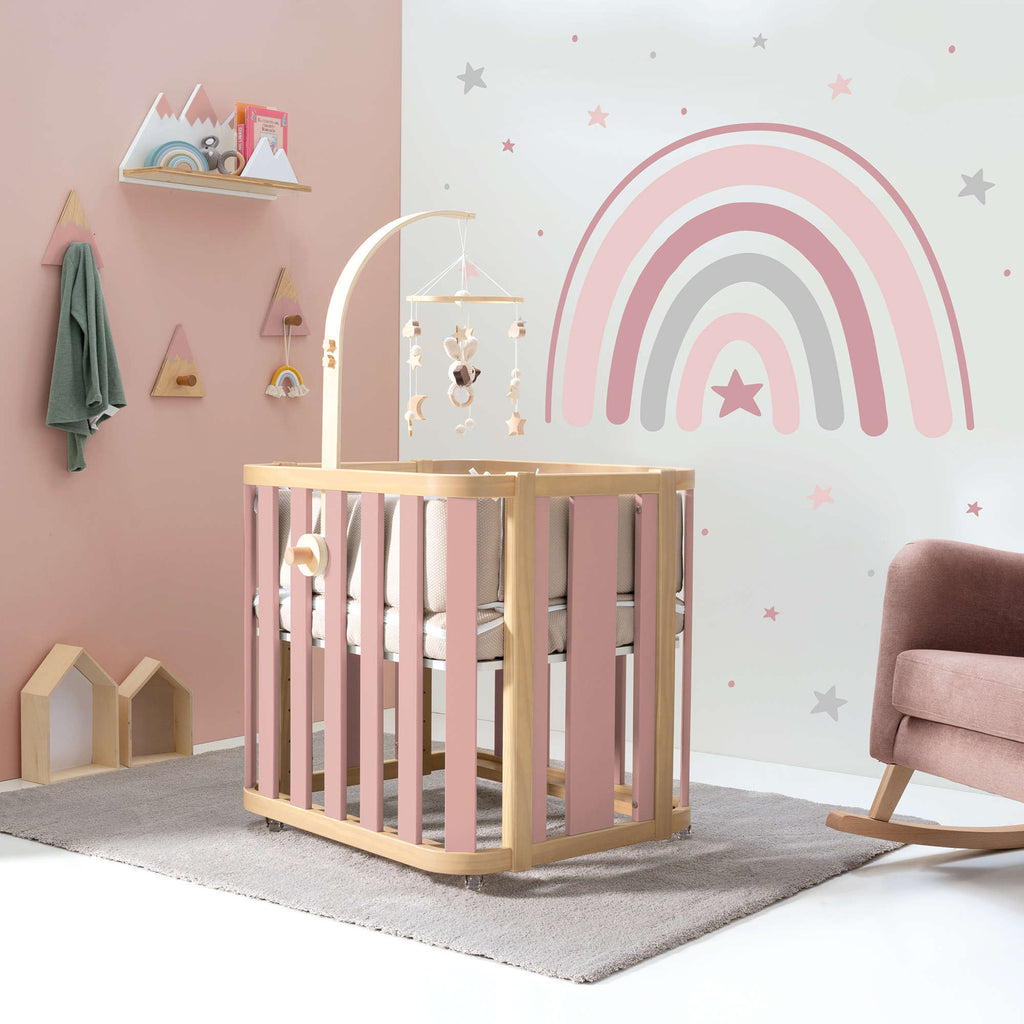 Habitación de bebé niña con minicuna en rosa/madera y mural de pared de arcoíris